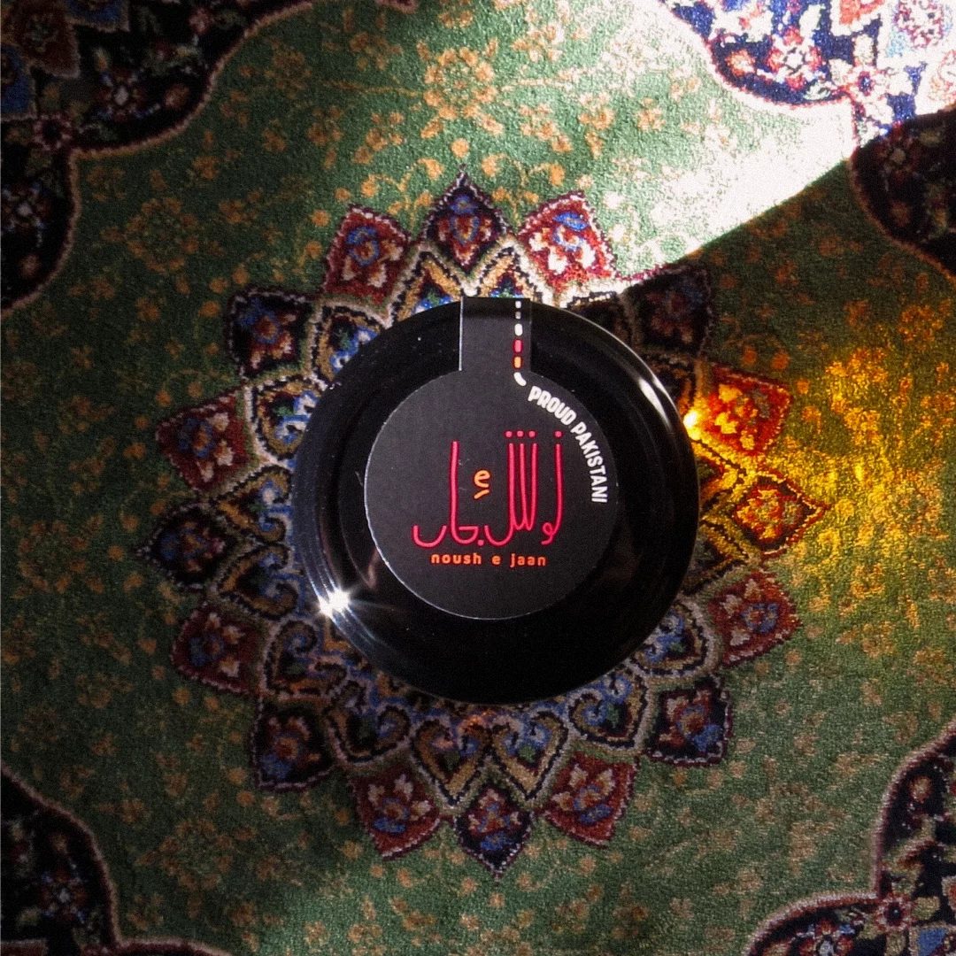 A row of Asal MINI jars on a dark reflective surface, each with a coloured label tab - Anaar, Keekar, Zeytoon.
